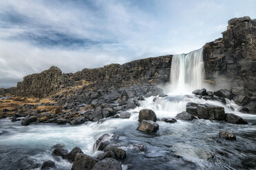 Scenic view of waterfall through rocky cliff against cloudy sky - CAVF15175