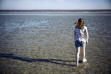 Rückansicht eines Mädchens, das an einem sonnigen Tag am Meeresufer spazieren geht - CAVF15193