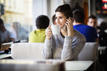 Happy woman using smart phone while drinking coffee at restaurant - CAVF15232