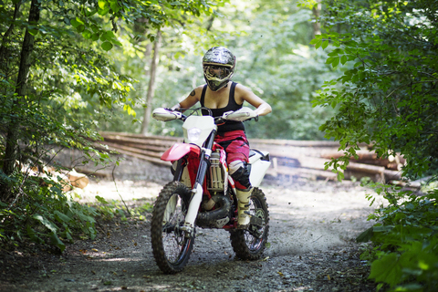 Junge Frau fährt Motorrad auf unbefestigtem Weg im Wald, lizenzfreies Stockfoto