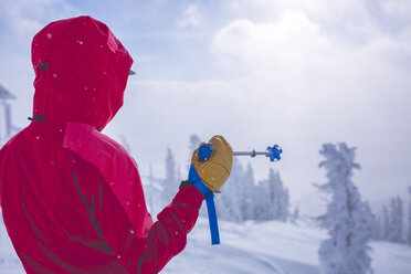 Rückansicht einer Frau, die einen Skistock hält, während sie auf einem verschneiten Feld steht - CAVF15251