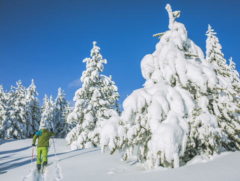 Mann beim Skifahren auf schneebedecktem Feld vor blauem Himmel in voller Länge, lizenzfreies Stockfoto