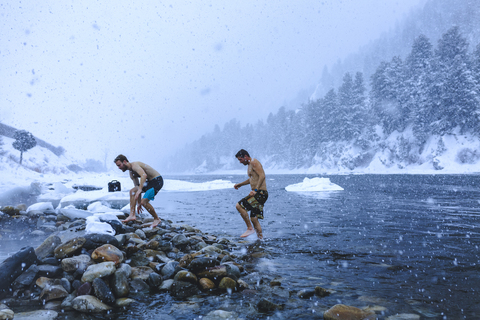 Männer, die bei Schneefall auf Steinen im Fluss laufen, lizenzfreies Stockfoto