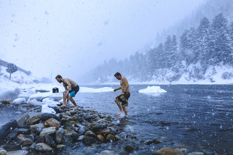 Men walking on stones in river during snowfall stock photo