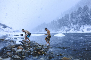 Männer, die bei Schneefall auf Steinen im Fluss laufen - CAVF15264