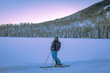 Tired female skier standing on snow covered field against trees - CAVF15278