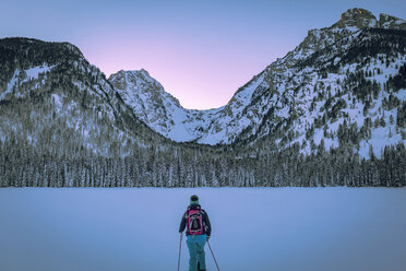 Rear view of woman with ski poles standing against snow covered mountains - CAVF15280