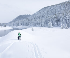 Rückansicht einer Wanderin, die auf einem schneebedeckten Feld gegen den Himmel wandert - CAVF15282