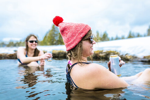 Happy female friends enjoying drinks in lake during winter - CAVF15287