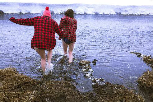 Rear view of female friends enjoying in lake during winter - CAVF15290