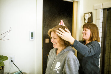 Frau benutzt Haarspray auf dem Haar ihrer Schwester - CAVF15292