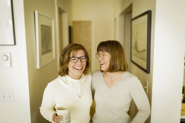 Cheerful siblings standing in corridor at home - CAVF15299