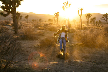 Verspielte Frau, die auf einem Feld im Joshua Tree National Park in den Sand tritt - CAVF15319