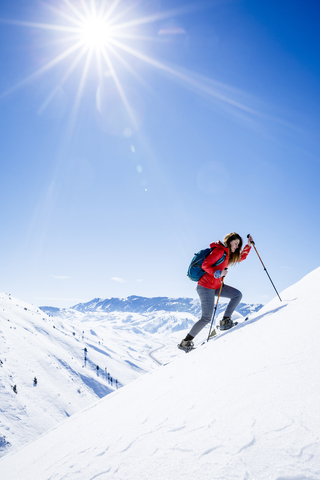 Female hiker climbing snow covered mountain against sky during sunny day stock photo