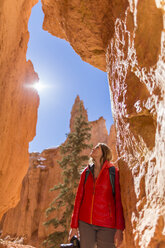 Low angle view of hiker looking up while standing by rock formations during sunny day - CAVF15337