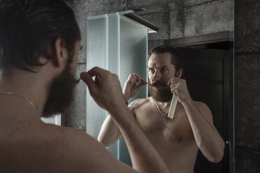 Portrait of bearded man looking at his mirror image while twirling his beard - VPIF00385