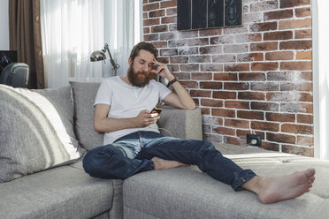 Mann mit Handy entspannt sich auf der Couch zu Hause - VPIF00389