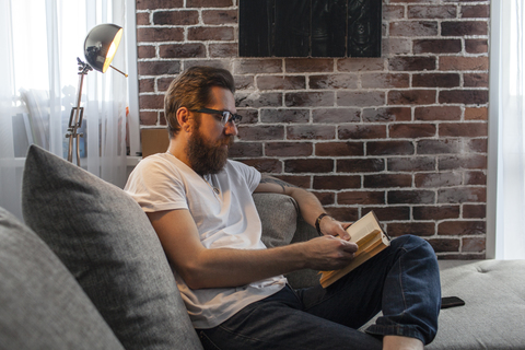 Man sitting on couch at home reading a book stock photo