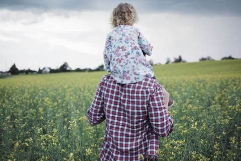 Rückansicht eines Vaters, der seine Tochter auf den Schultern trägt, auf einem Feld gegen den Himmel, lizenzfreies Stockfoto