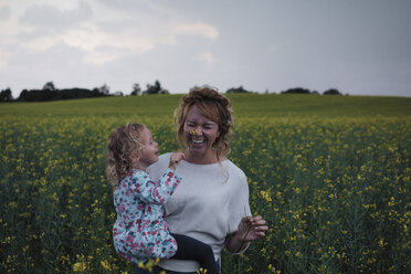 Tochter berührt Blume auf der Nase der fröhlichen Mutter auf einem Feld gegen den Himmel - CAVF15347