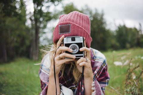 Frau fotografiert mit Sofortbildkamera auf einer Wiese, lizenzfreies Stockfoto