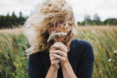 Frau mit zerzaustem Haar hält Blumen auf einem Feld - CAVF15355