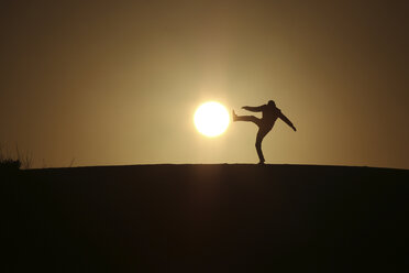 Optical illusion of silhouette man kicking sun during sunset - CAVF15369