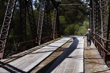 Junge hält Angelruten beim Spaziergang auf einer Brücke an einem sonnigen Tag - CAVF15374