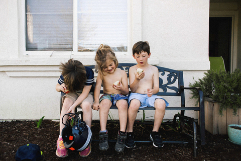 Geschwister essen Äpfel, während sie auf einer Bank im Hinterhof sitzen, lizenzfreies Stockfoto