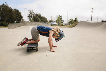 Verspieltes Mädchen kniend auf Skateboard im Park - CAVF15384