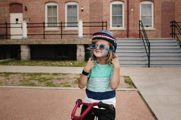 Happy girl wearing goggles while standing with bicycle - CAVF15387