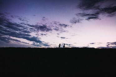 Silhouette Geschwister laufen auf Feld gegen Himmel bei Sonnenuntergang - CAVF15390
