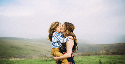 Liebende Frau, die ihre Tochter küsst, während sie auf einem Feld vor dem Himmel steht - CAVF15393