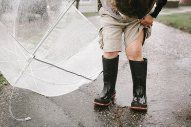 Mädchen in Gummistiefeln hält Regenschirm, während sie auf nasser Straße steht - CAVF15406