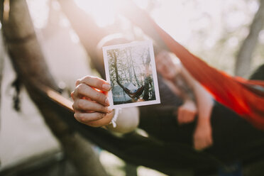 Mann hält ein Foto in der Hand, während er sich in der Hängematte an einem sonnigen Tag entspannt - CAVF15422