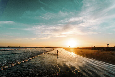 Rückansicht von Menschen, die bei Sonnenuntergang am Ufer laufen - CAVF15433