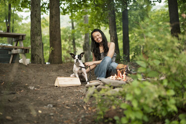 Porträt einer glücklichen Frau, die mit einem Boston Terrier im Wald sitzt - CAVF15463