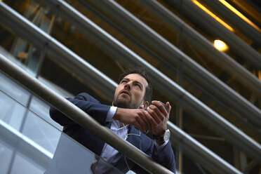 Low angle view of businessman looking away while listening music by railing - CAVF15478