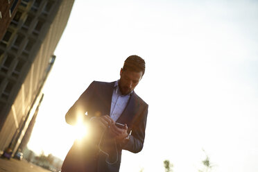 Low angle view of businessman using mobile phone while standing against clear sky - CAVF15483