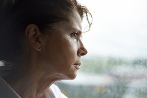 Nachdenkliche Frau schaut durch das Fenster, während sie zu Hause steht, lizenzfreies Stockfoto