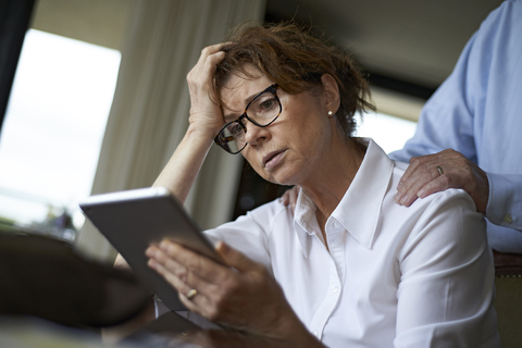 Frau benutzt Tablet-Computer, während ihr Mann im Hintergrund steht, lizenzfreies Stockfoto