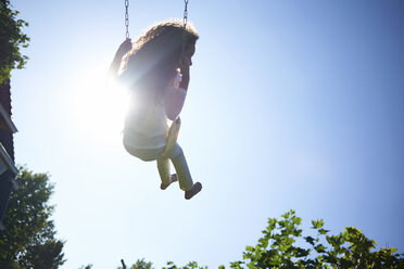 Low angle view of girl swinging against blue sky in backyard - CAVF15511