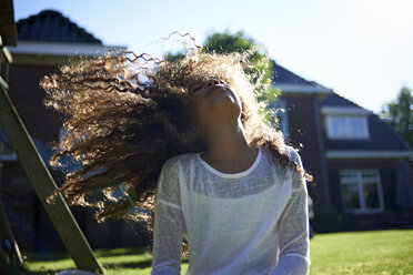 Happy girl shaking head while standing against house in backyard - CAVF15512