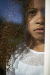 Mädchen, das wegschaut, während es zu Hause steht, gesehen durch ein Fensterglas - CAVF15514