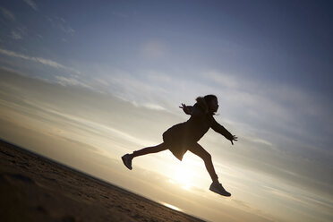 Happy girl jumping at beach against sky during sunset - CAVF15519