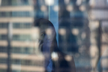 Spiegelung einer Geschäftsfrau, die ihr Smartphone bedient, gesehen am Fenster im Büro - CAVF15539