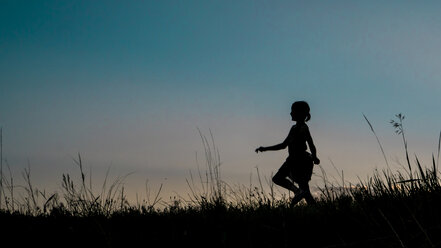 Silhouette Mädchen zu Fuß auf grasbewachsenen Feld gegen klaren Himmel in der Abenddämmerung - CAVF15546