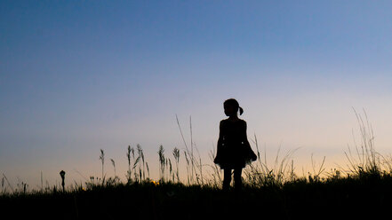 Silhouette Mädchen stehend auf grasbewachsenem Feld gegen klaren Himmel in der Abenddämmerung - CAVF15547