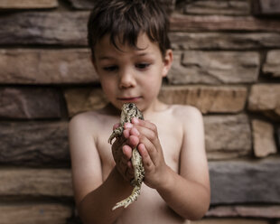 Verspielter Junge hält Frosch, während er an der Wand steht - CAVF15550