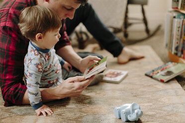 Father showing picture book to son while sitting on carpet at home - CAVF15561